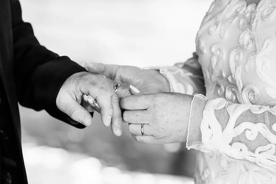 A couple holding hands while the bride puts on the grooms ring, in black and white
