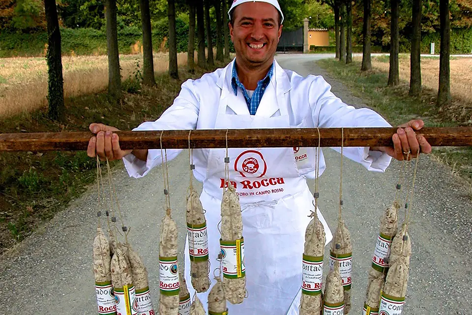 A Salumificio La Rocca man holding Coppa, Salame and Pancetta Piacentina on a stick